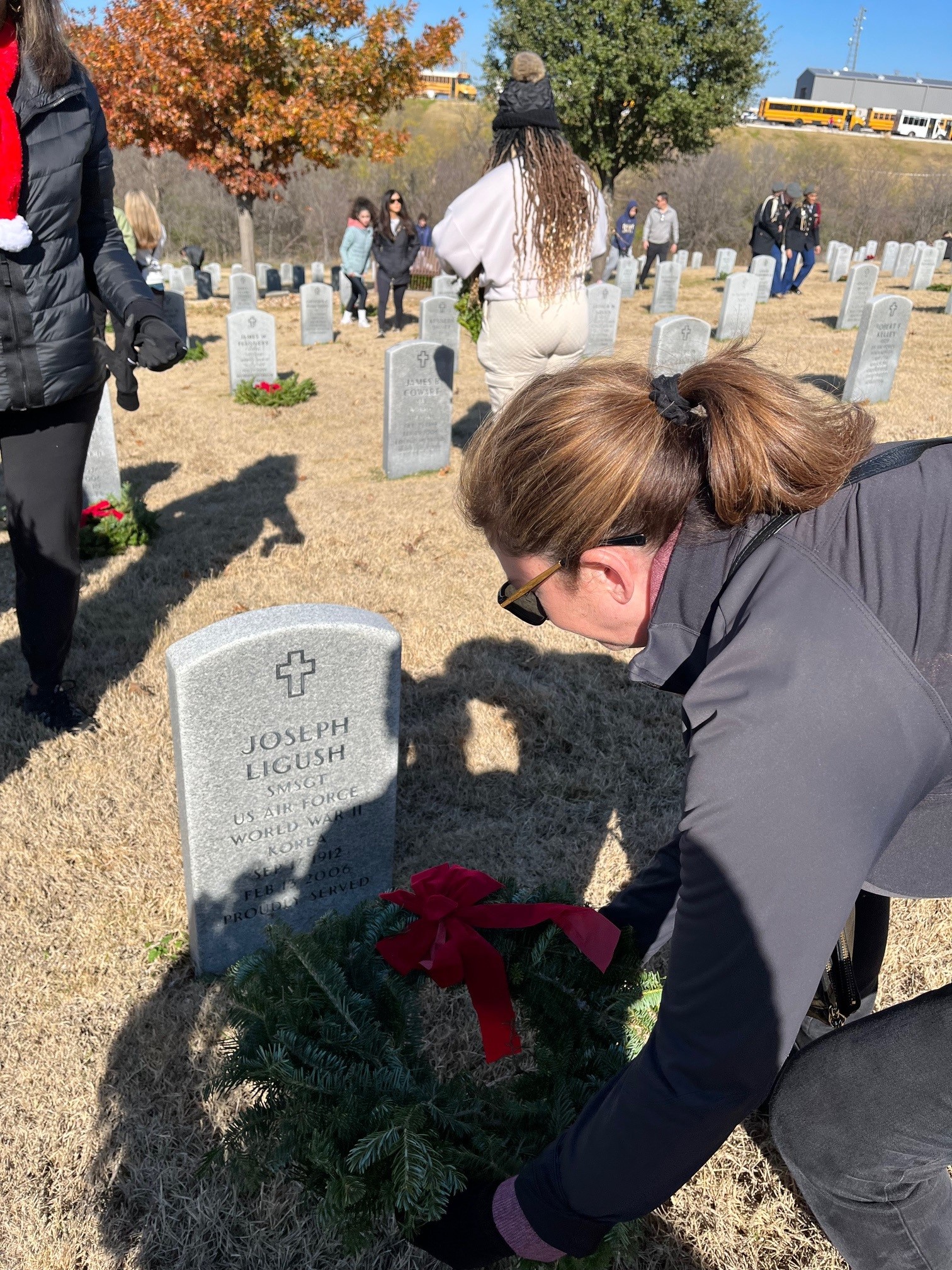 woman lays down wreath at gravestone